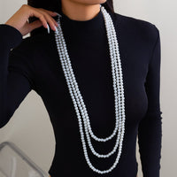 Thumbnail for A woman wearing a black long-sleeve top and a layered pearl necklace with a long chain design.