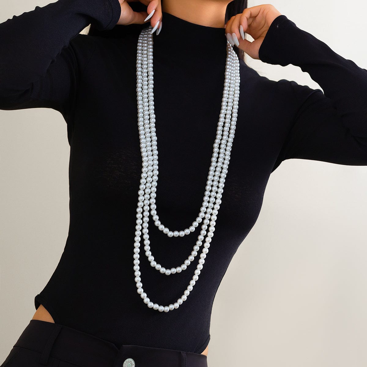 A woman wearing a black long-sleeve top and a layered pearl necklace with a long chain design.