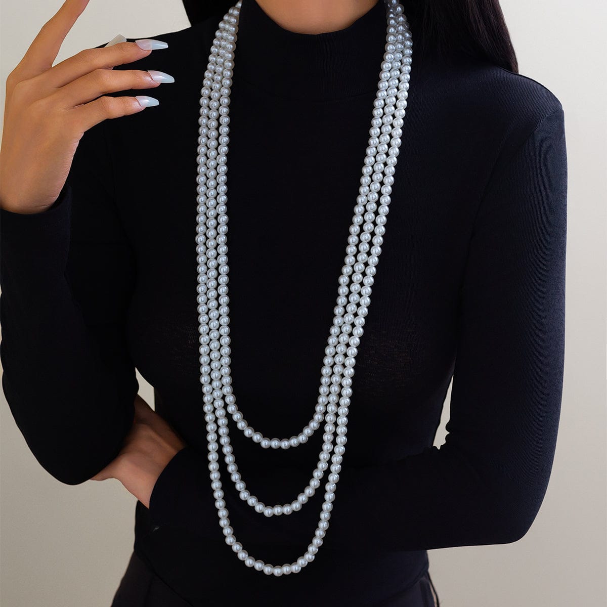 A woman wearing a black long-sleeve top and a layered pearl necklace with a long chain design.
