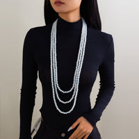 Thumbnail for A woman wearing a black long-sleeve top and a layered pearl necklace with a long chain design.