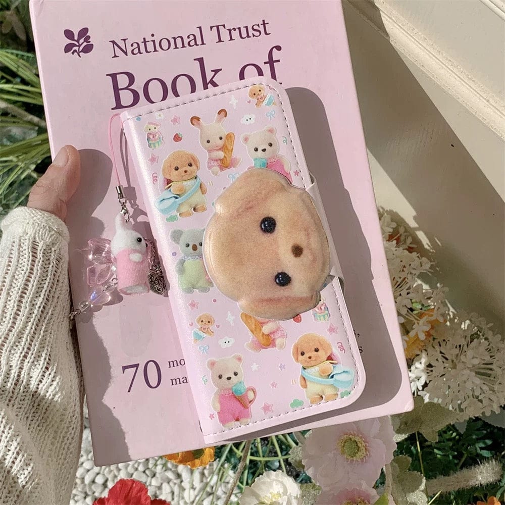 A person holding a pink iPhone case with a Sylvanian Families theme, featuring character illustrations and a small charm.