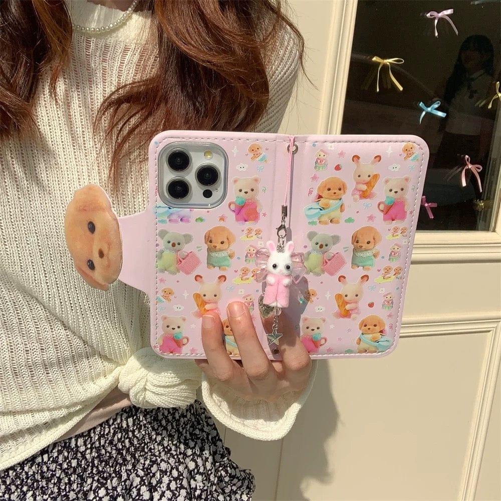 A person holding a pink iPhone case with a Sylvanian Families theme, featuring character illustrations and a small charm.