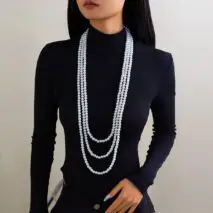 A woman wearing a black long-sleeve top and a layered pearl necklace with a long chain design.
