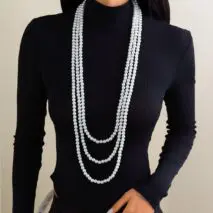 A woman wearing a black long-sleeve top and a layered pearl necklace with a long chain design.