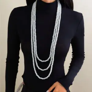 A woman wearing a black long-sleeve top and a layered pearl necklace with a long chain design.