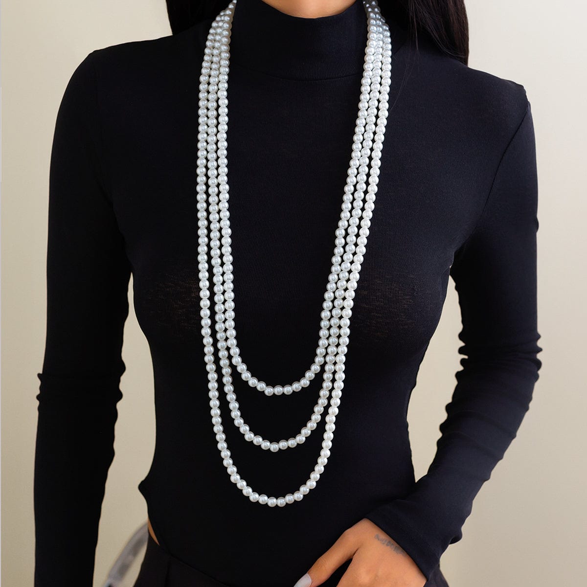 A woman wearing a black long-sleeve top and a layered pearl necklace with a long chain design.