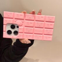 A person holding a chocolate-colored silicone iPhone case featuring Rilakkuma and Hello Kitty characters.