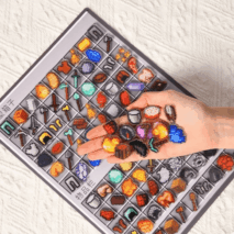 Hand holding colorful miniature items above a tray with similar items on a textured surface